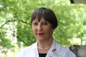 Portrait einer Frau mit Kurzhaarschnitt und Perlenkette vor Bäumen