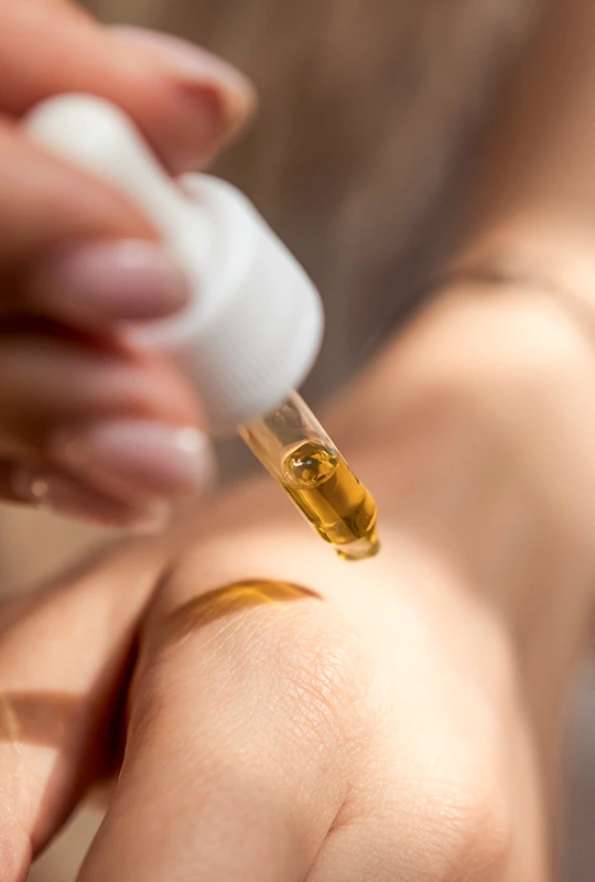 Frau träufelt mit einer Pipette Öl auf ihre Handaussenseite