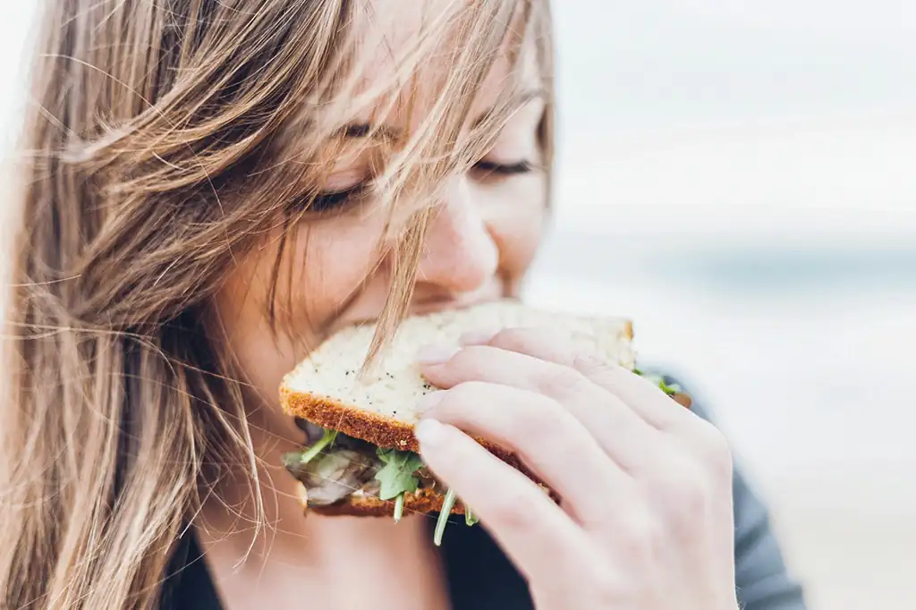 Une femme croque à pleines dents dans un sandwich sain de goûter